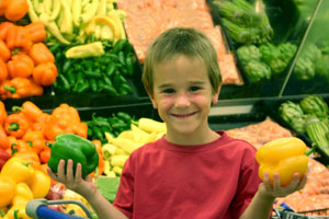 Boy in green grocers holding peppers